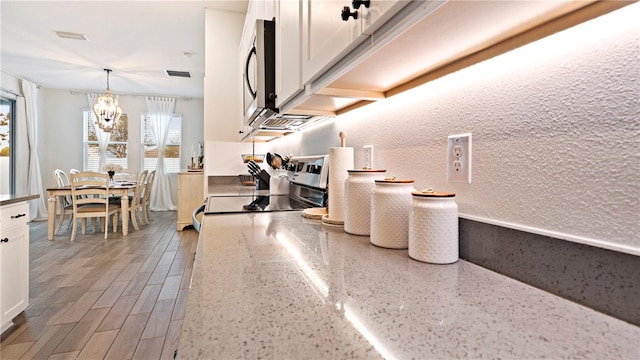 kitchen with light stone counters, white cabinets, stainless steel appliances, and decorative light fixtures