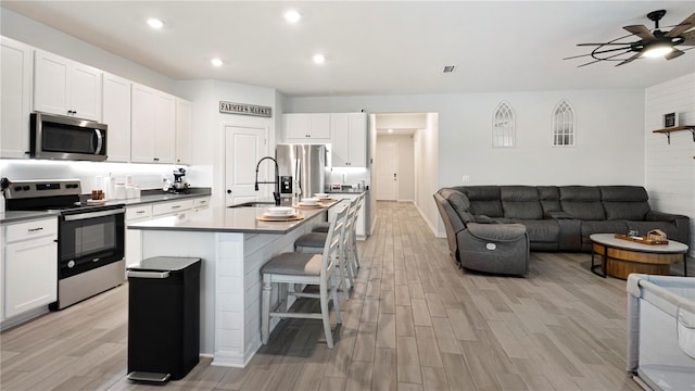 kitchen with white cabinetry, stainless steel appliances, a kitchen island with sink, and light hardwood / wood-style flooring