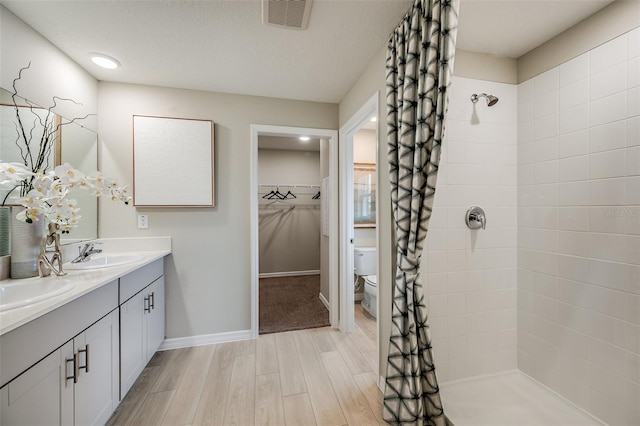 bathroom featuring tiled shower, toilet, vanity, and hardwood / wood-style flooring