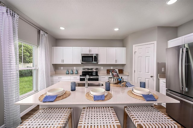 kitchen featuring appliances with stainless steel finishes, a center island with sink, white cabinetry, and plenty of natural light