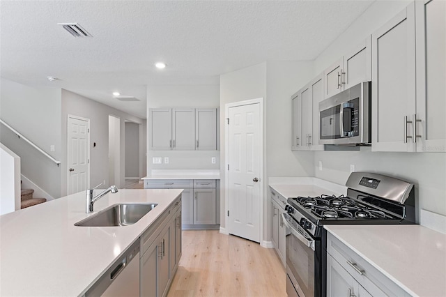 kitchen with stainless steel appliances, a textured ceiling, sink, and light hardwood / wood-style floors