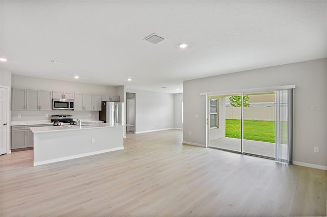 kitchen featuring stainless steel appliances, sink, light wood-type flooring, gray cabinets, and a center island with sink