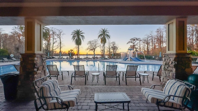 patio terrace at dusk featuring a community pool