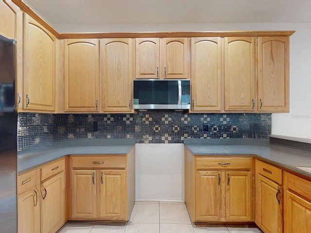 kitchen featuring light brown cabinets, backsplash, black fridge, and light tile patterned flooring