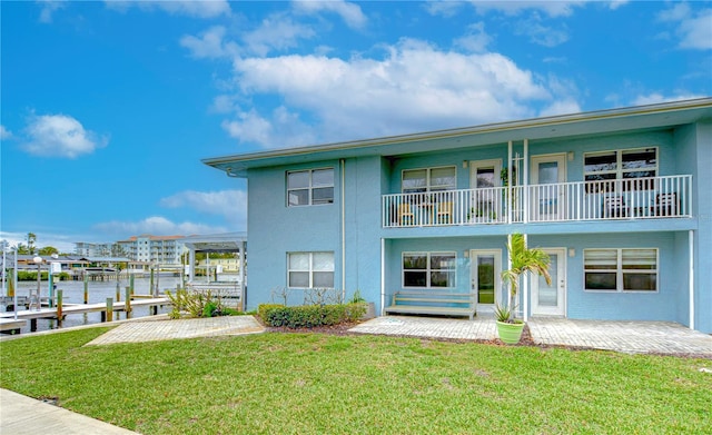 view of front facade with stucco siding, a front yard, a patio area, a boat dock, and a balcony