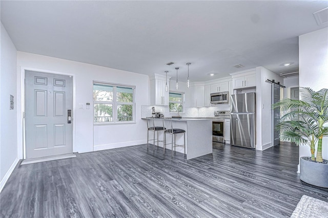 kitchen featuring a barn door, decorative backsplash, dark wood-style flooring, stainless steel appliances, and a kitchen bar