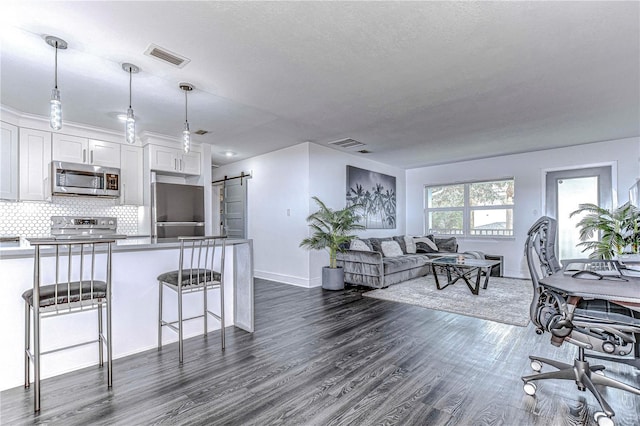 kitchen with a barn door, dark wood-type flooring, visible vents, appliances with stainless steel finishes, and tasteful backsplash