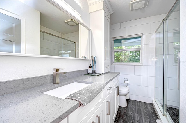 bathroom with tile walls, toilet, a stall shower, vanity, and wood finished floors