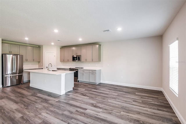 kitchen featuring stainless steel appliances, a healthy amount of sunlight, sink, dark hardwood / wood-style floors, and an island with sink