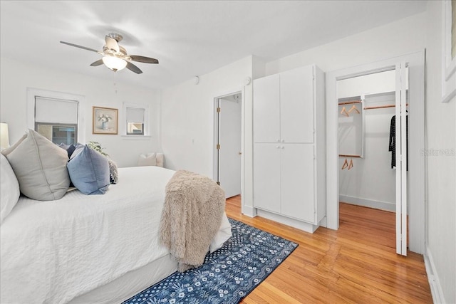 bedroom with a spacious closet, a closet, ceiling fan, and light wood-type flooring