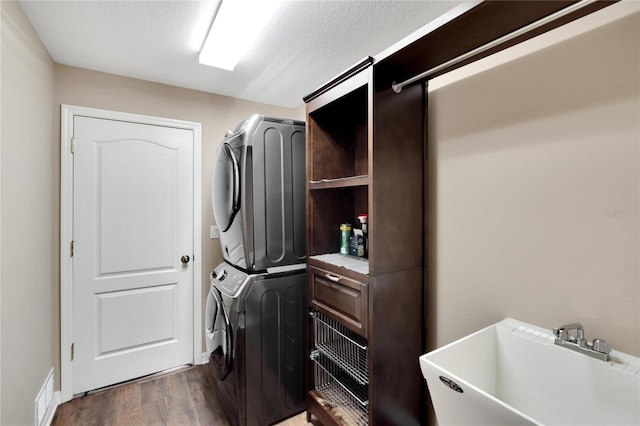 washroom featuring stacked washing maching and dryer, dark hardwood / wood-style flooring, sink, and a textured ceiling