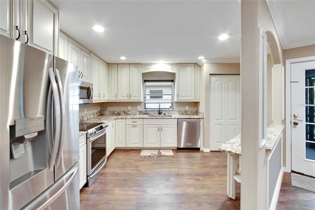 kitchen featuring sink, crown molding, dark hardwood / wood-style floors, stainless steel appliances, and light stone countertops