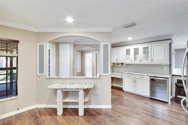 kitchen with white cabinetry, backsplash, wine cooler, light stone counters, and a kitchen bar