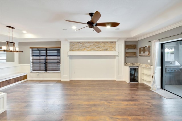 unfurnished living room with crown molding, dark wood-type flooring, ceiling fan with notable chandelier, and beverage cooler