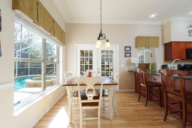 dining space with ornamental molding, french doors, an inviting chandelier, and light wood-type flooring