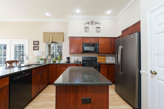 kitchen featuring dark stone countertops, black appliances, crown molding, a kitchen island, and sink