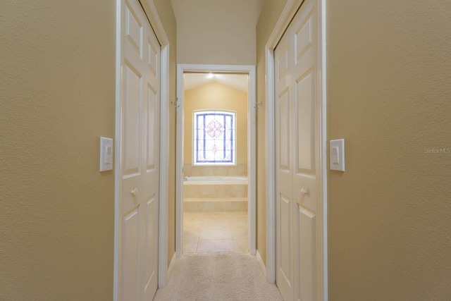 hallway featuring lofted ceiling and light colored carpet