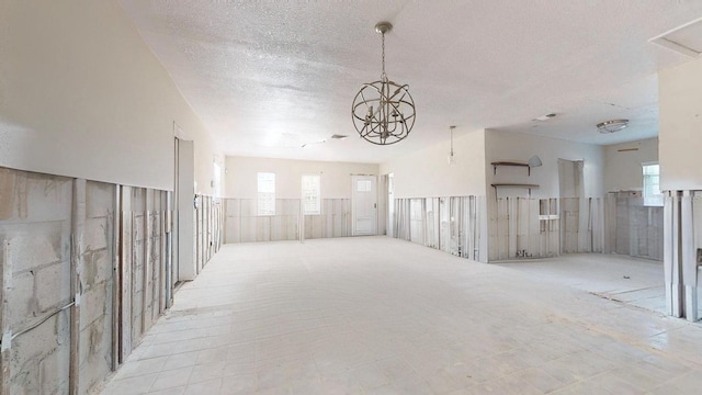 unfurnished room with a healthy amount of sunlight, a textured ceiling, and an inviting chandelier