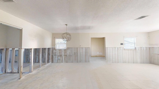 empty room with a healthy amount of sunlight, a textured ceiling, and an inviting chandelier