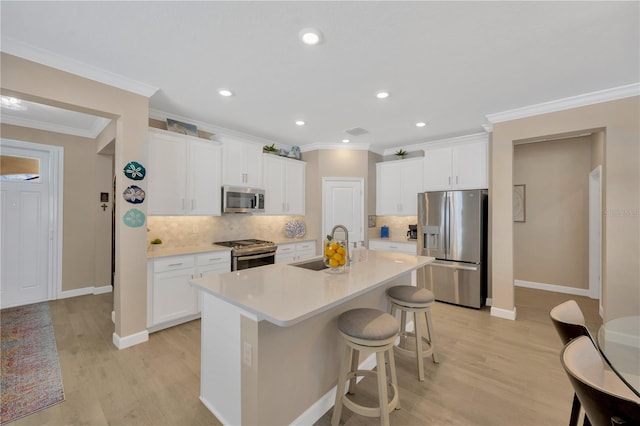 kitchen featuring appliances with stainless steel finishes, decorative backsplash, a kitchen island with sink, white cabinets, and sink