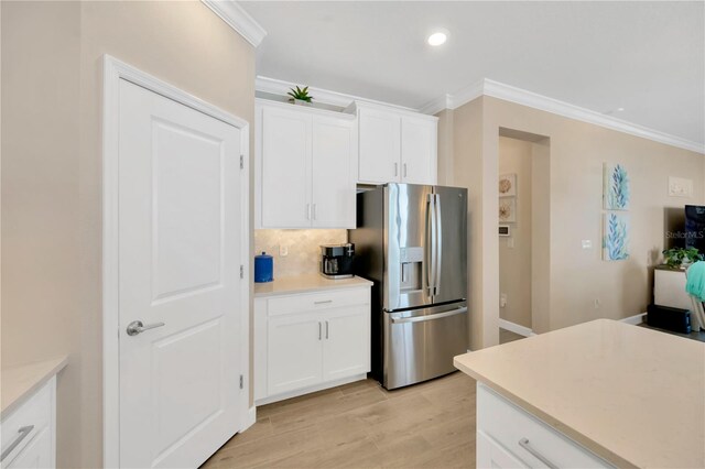 kitchen with stainless steel refrigerator with ice dispenser, ornamental molding, white cabinets, and light wood-type flooring