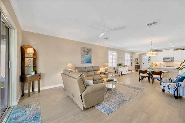 living room with light wood-type flooring, ceiling fan, and crown molding