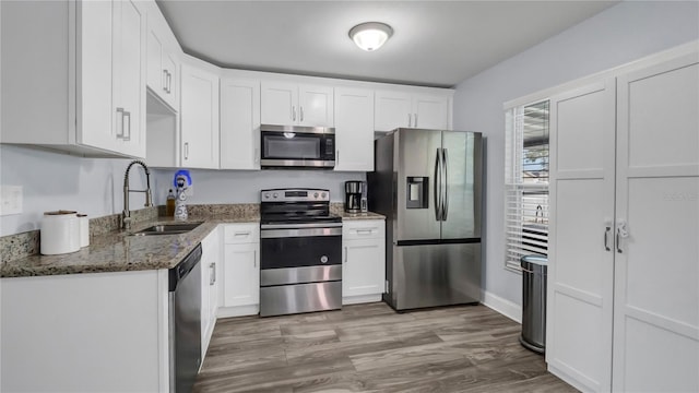 kitchen featuring dark stone countertops, appliances with stainless steel finishes, white cabinets, light hardwood / wood-style flooring, and sink