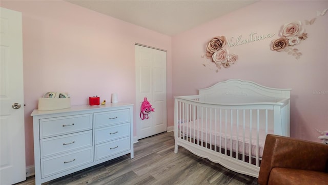 bedroom with a closet, a crib, and wood-type flooring