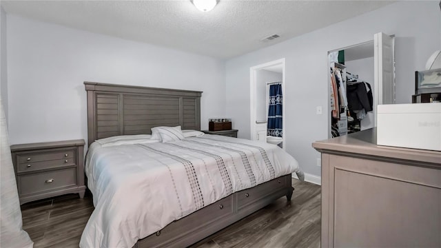 bedroom with a textured ceiling, ensuite bath, a closet, a walk in closet, and dark hardwood / wood-style flooring