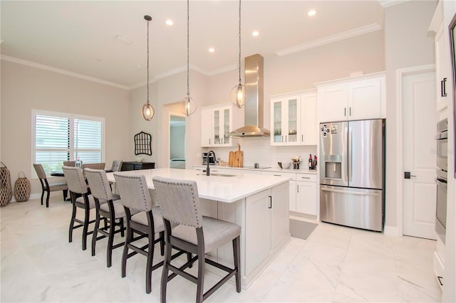 kitchen with stainless steel refrigerator with ice dispenser, wall chimney range hood, white cabinets, and an island with sink