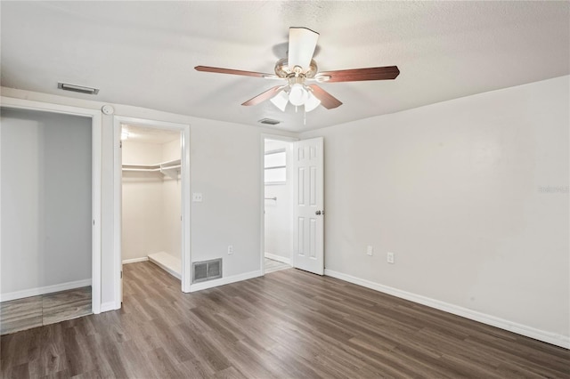 unfurnished bedroom with wood-type flooring, a walk in closet, ceiling fan, and a closet