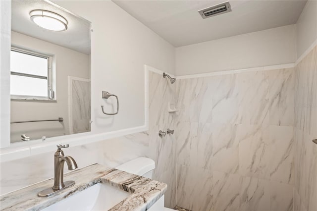 bathroom featuring vanity, a tile shower, and toilet