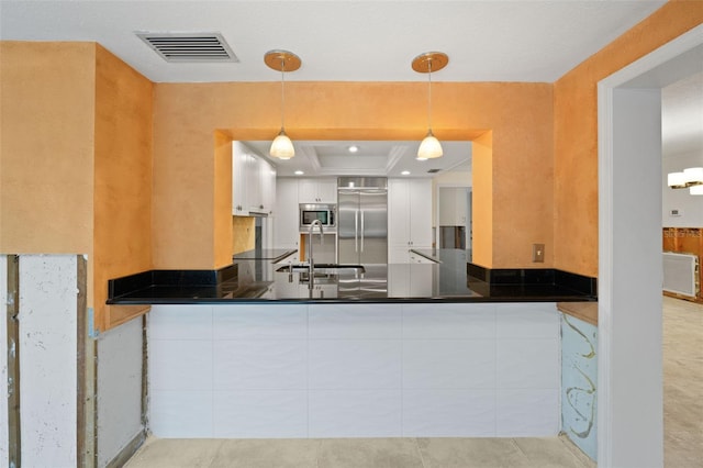 kitchen featuring built in appliances, decorative light fixtures, a tray ceiling, white cabinetry, and sink