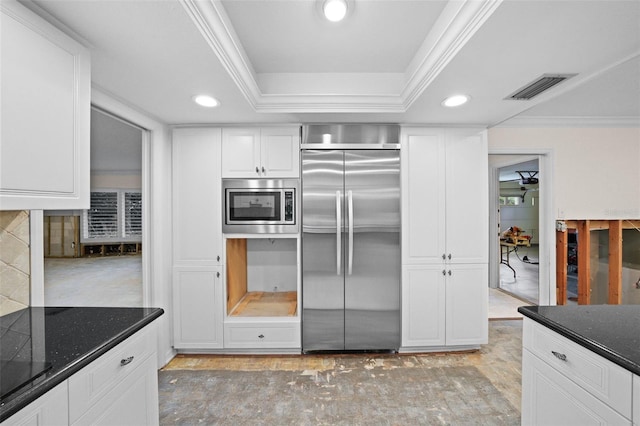 kitchen with built in appliances, ornamental molding, white cabinets, dark stone counters, and ceiling fan