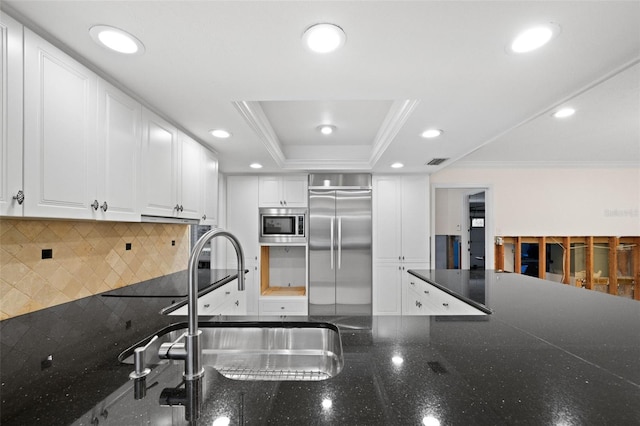 kitchen with built in appliances, white cabinets, a raised ceiling, decorative backsplash, and crown molding