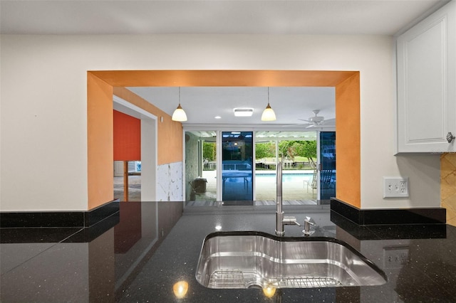 kitchen with white cabinets, ceiling fan, pendant lighting, and dark stone counters