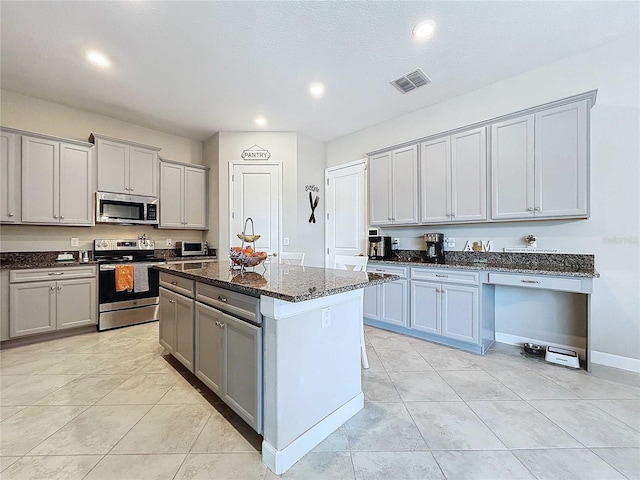 kitchen featuring gray cabinetry, a kitchen island, dark stone countertops, and stainless steel appliances