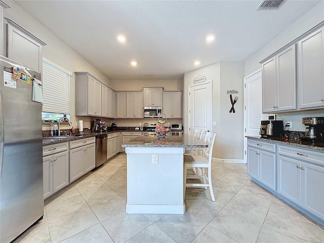 kitchen with gray cabinetry, a center island, stainless steel appliances, dark stone counters, and light tile patterned flooring