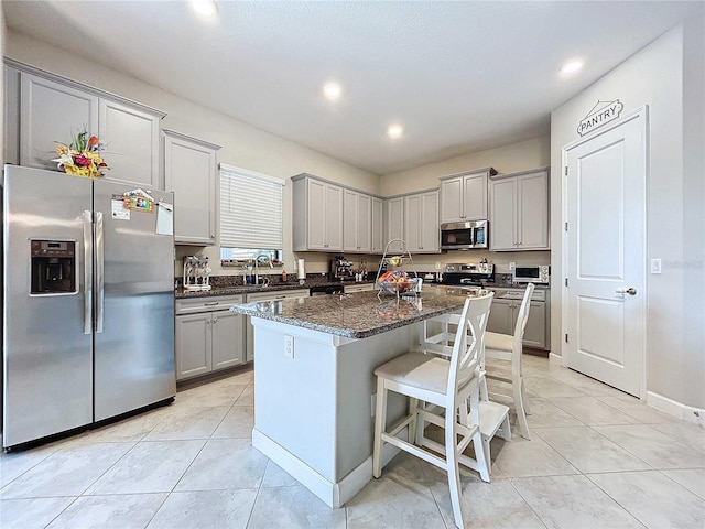 kitchen with sink, dark stone countertops, appliances with stainless steel finishes, a kitchen island, and a breakfast bar area