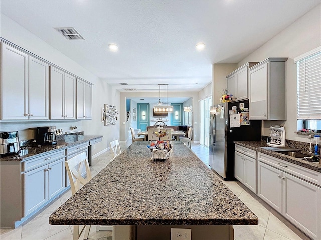 kitchen featuring stainless steel refrigerator, dark stone countertops, a kitchen island, and decorative light fixtures