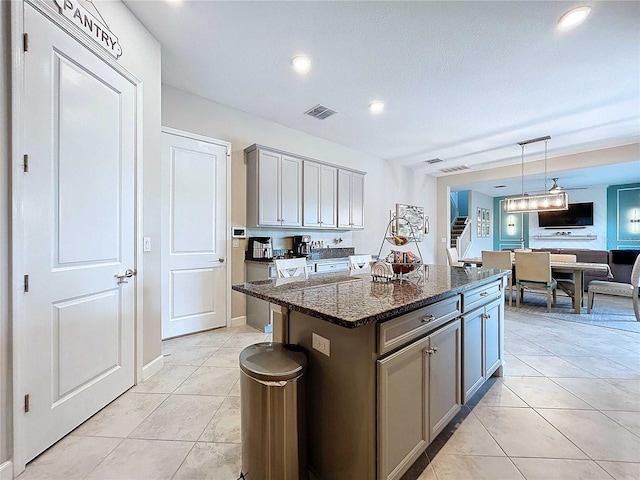 kitchen featuring gray cabinetry, a center island, dark stone counters, decorative light fixtures, and light tile patterned flooring