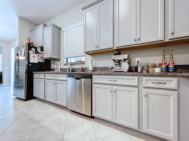 kitchen with appliances with stainless steel finishes, light tile patterned floors, and dark stone countertops