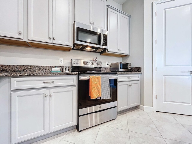 kitchen with appliances with stainless steel finishes, dark stone counters, and light tile patterned flooring