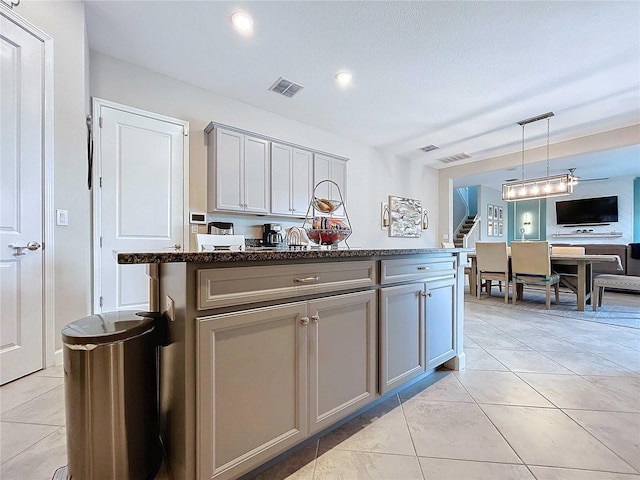 kitchen with light tile patterned flooring, hanging light fixtures, gray cabinets, dark stone countertops, and a kitchen island