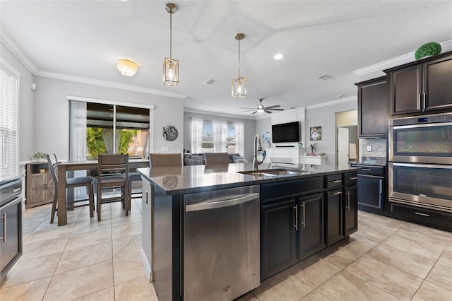 kitchen with stainless steel appliances, sink, ceiling fan, dark stone counters, and a center island with sink