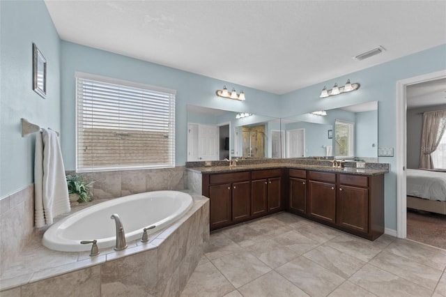 bathroom with tile patterned flooring, a relaxing tiled tub, and vanity