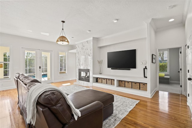 living room with a multi sided fireplace, light hardwood / wood-style floors, a textured ceiling, french doors, and ornamental molding