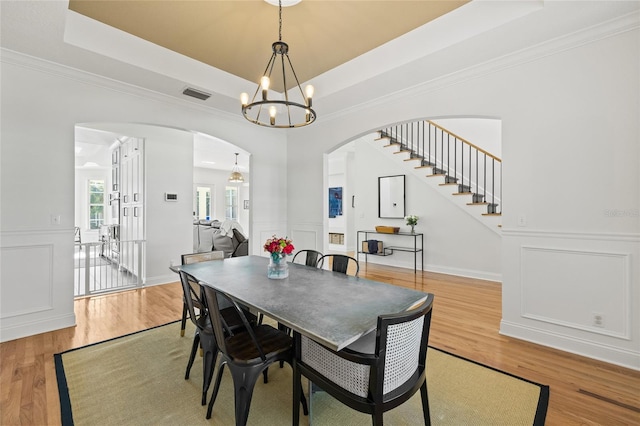 dining area featuring wood-type flooring, ornamental molding, a raised ceiling, and a chandelier