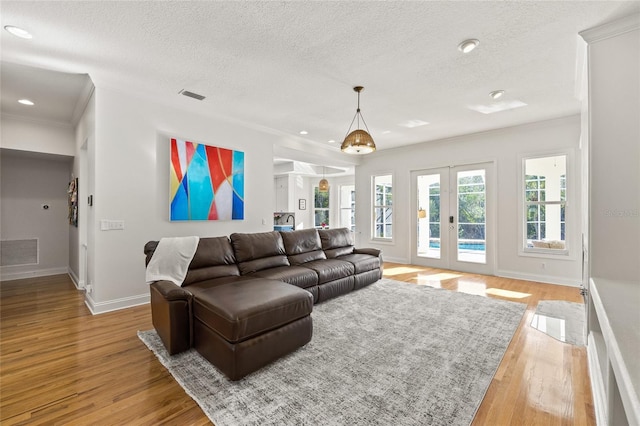 living room with a textured ceiling, ornamental molding, french doors, and light wood-type flooring