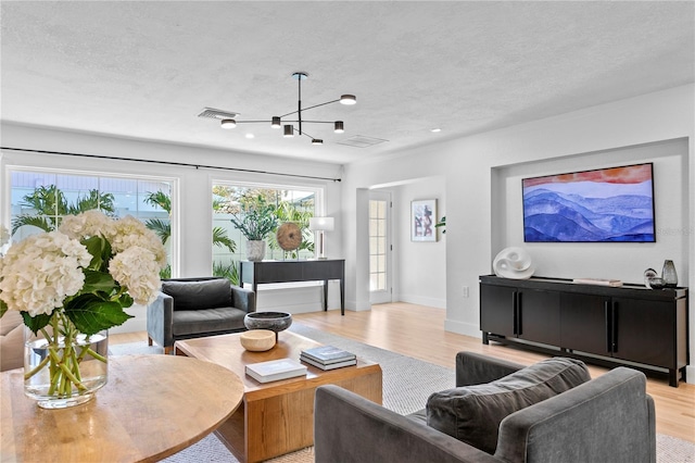 living room with a notable chandelier, a textured ceiling, and light wood-type flooring